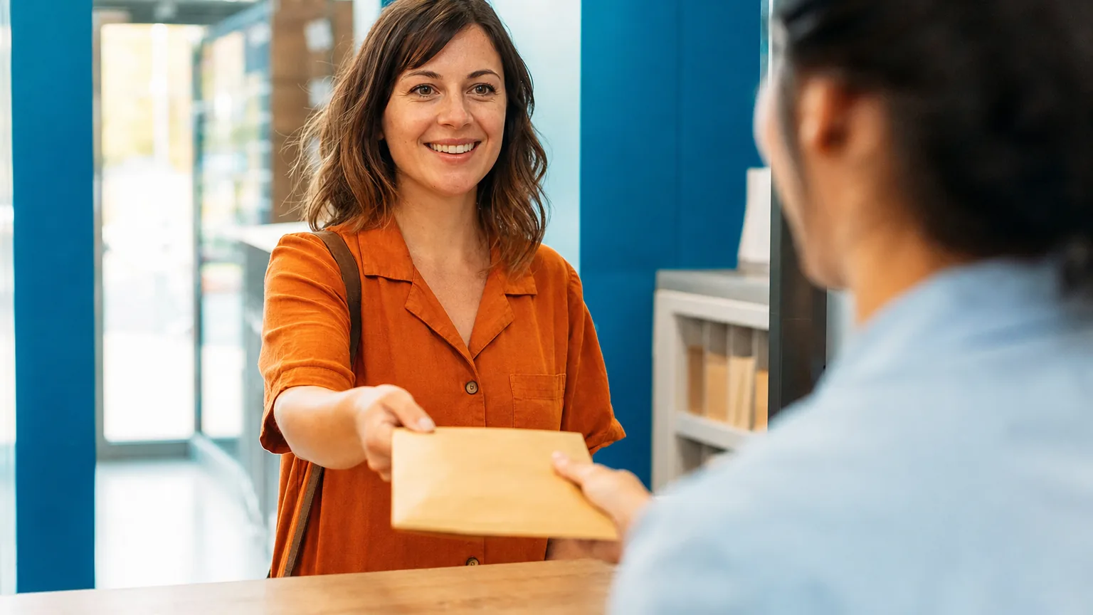 A smiling woman handing an envelope directly to another person