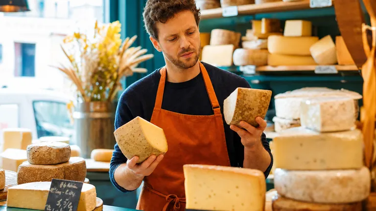 A cheesemonger holding up two pieces of cheese at his market stall